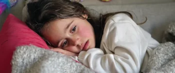 A young girl lies quietly on a couch, her face turned toward the camera, reflecting sadness and longing. Agape Villages helps children like her find safety and hope through caring foster families.