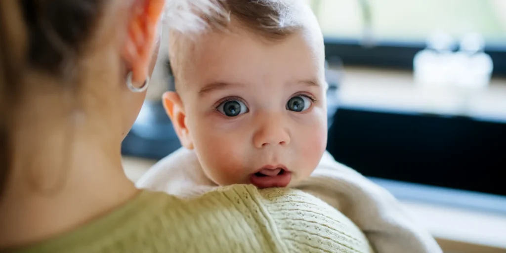 Close up of a 4 month old foster child's face looking over the shoulder of an older girl's shoulder holding the child.